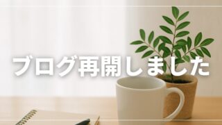 明るいデスクにノート、白いマグカップ、観葉植物が並ぶ写真