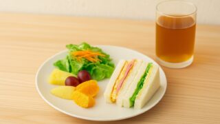 軽めのサンドイッチ、フルーツ、サラダと薄い色の麦茶の写真